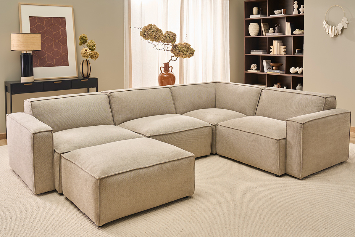 Canap� d'angle beige 5 places avec pouf, effet velours, dans un salon moderne.