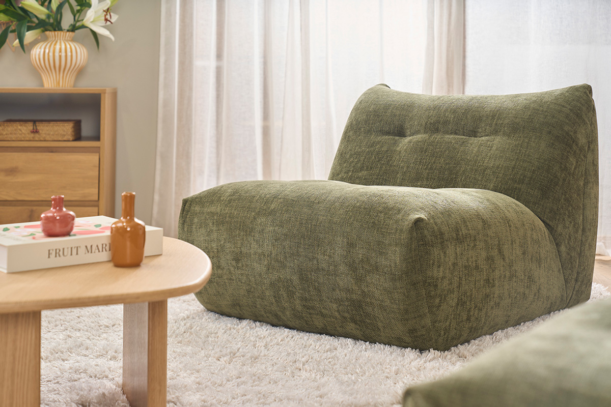Fauteuil lounge BUMPY en tissu vert kaki, vue de 3/4, avec table basse en bois et accessoires d�coratifs.
