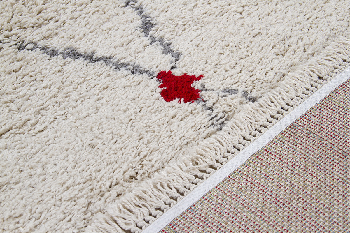 Zoom sur un tapis LIO, texture �paisse avec motif losange gris et touche rouge, franges sur le c�t�.